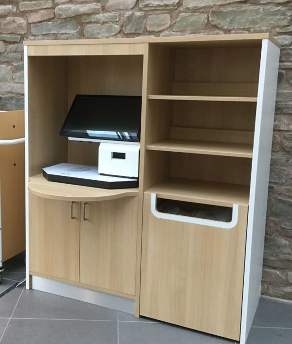 Light wood kiosk housing with a computer screen, printer, and open shelving at Brecon Library
