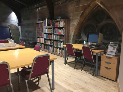Light wood study tables and burgundy upholstered chairs in a local studies area with stone walls at Lichfield Local Studies