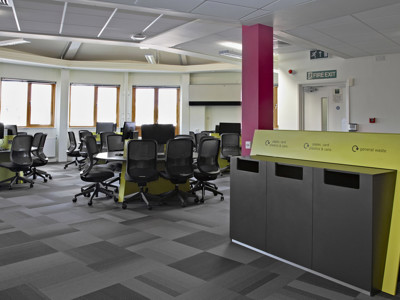 Black office chairs and collaborative work tables in a study area with green accents at Boots Library