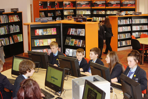 Six students engaged at computer stations in a collaborative work area with colourful book displays at Carleton High School