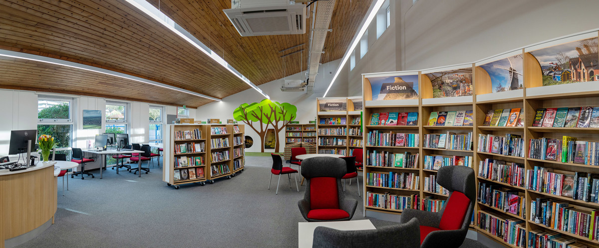 Red and grey upholstered chairs beside colourful browsing shelves in a public library browsing area at Chinnor Library