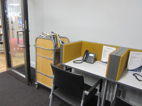 Study desk with a telephone and partitioned space beside a book trolley at Morley Library