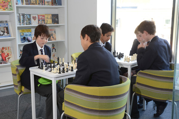 Green and grey upholstered chairs surrounding white study tables where students engage in chess games at King Edward's School