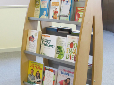 Curved wooden browsing shelves displaying health and wellbeing books in a public library browsing area at Lees Library