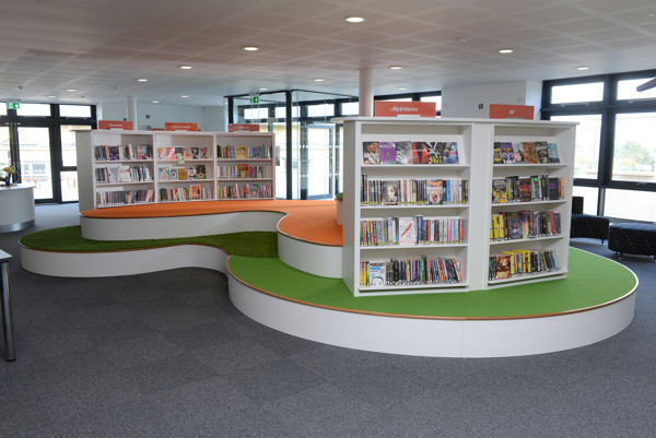 Curved shelving units with colourful book displays on orange and green carpeted platforms in a young readers' browsing space at King Edward's School