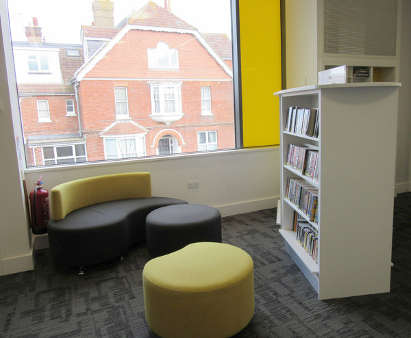 Curved black and yellow seating with a low round ottoman beside a white book display at Seaford Library