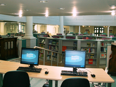 Two computer workstations with keyboards facing a browsing area filled with bookshelves at St Aubyn Library Church