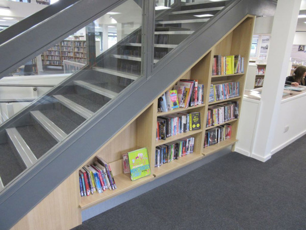 Custom shelving built under a staircase displaying books and DVDs in a public library browsing area at Arnold Library