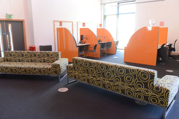 Patterned green and yellow sofas in a public library browsing area with orange advice desks at Southwater Customer Services