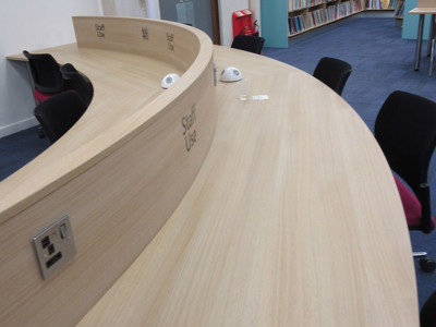 Curved wooden counter with power access and seating for staff at County Library