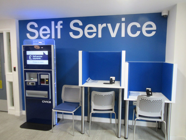 Self-service kiosk and blue privacy booths with chairs in the advice area at Midsomer Norton Library