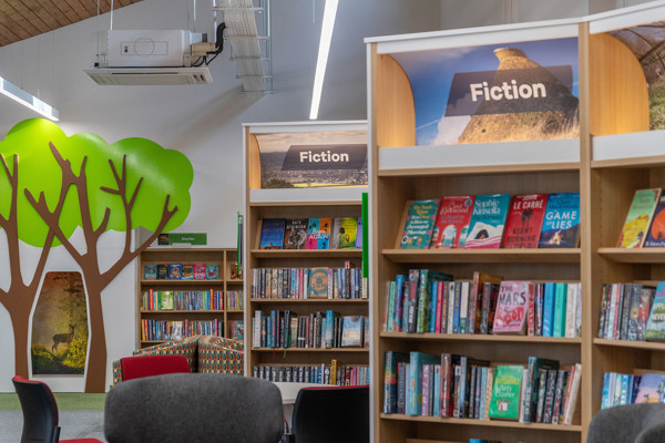 Colourful book displays featuring fiction titles beside a tree mural in the browsing area at Chinnor Library