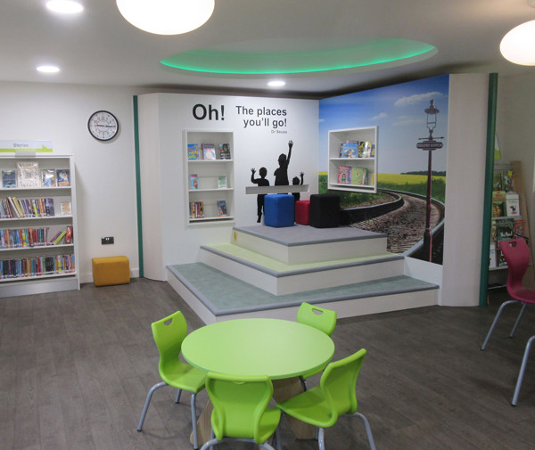 Bright green tables and colourful stools in a children's reading area featuring playful wall graphics at Midsomer Norton Library