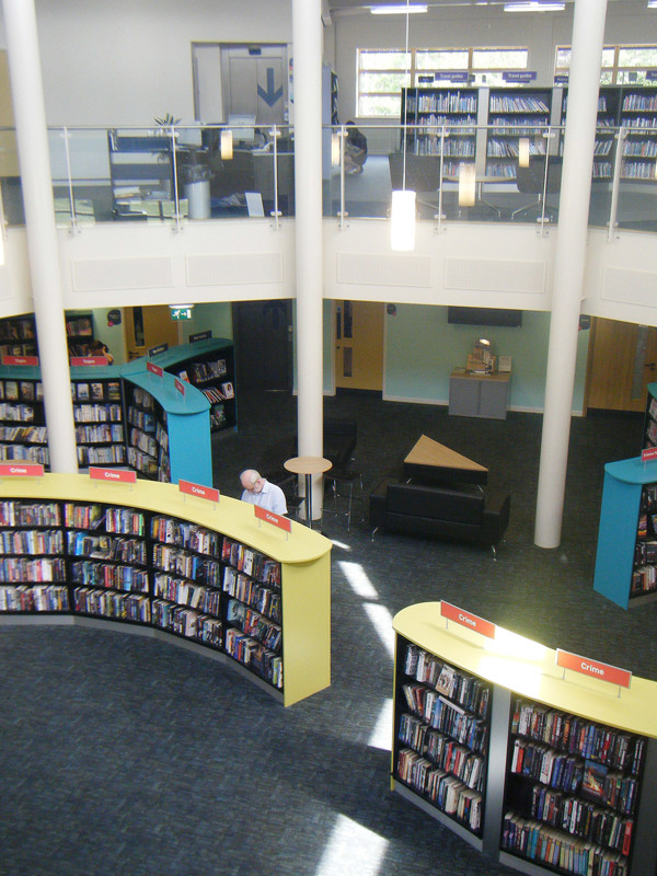 Curved browsing shelves in yellow and turquoise with a study area and seating at Worksop Library