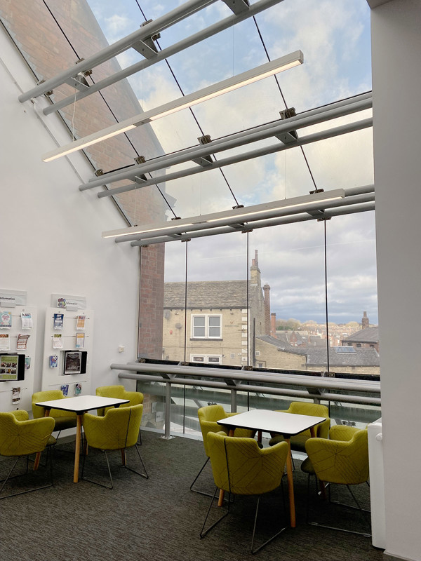 Light-filled study area with yellow upholstered chairs and white tables overlooking the cityscape at Armley Library