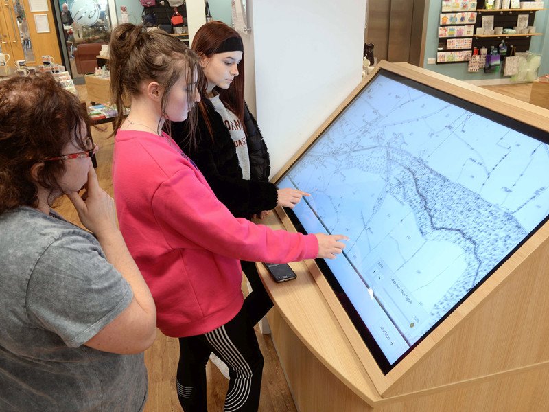 Three young adults interacting with a large touchscreen display in a digital information area at Gateshead Archive Library