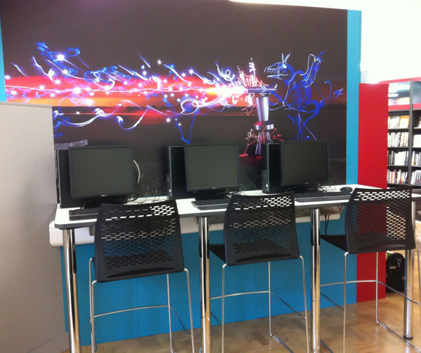 Black mesh stools and computer stations against a vibrant graphic wall at Newbridge Library