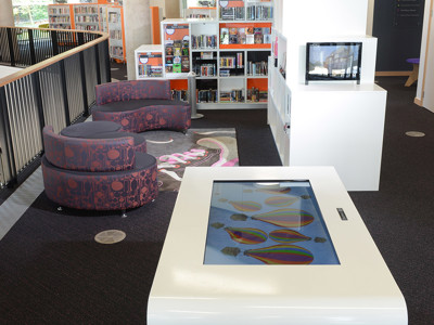 Interactive touchscreen table and purple upholstered seating in a digital engagement area at Southwater Library