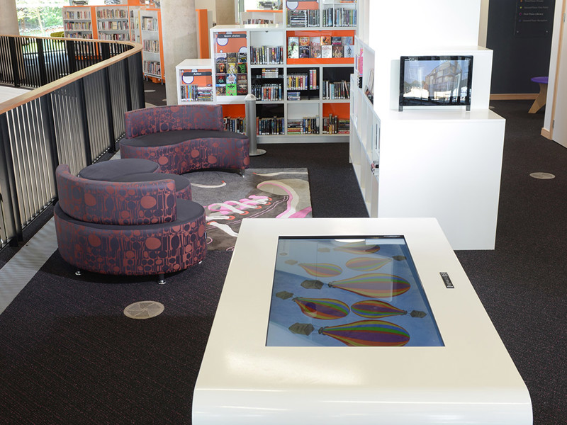 Interactive touchscreen table and purple upholstered seating in a digital engagement area at Southwater Library