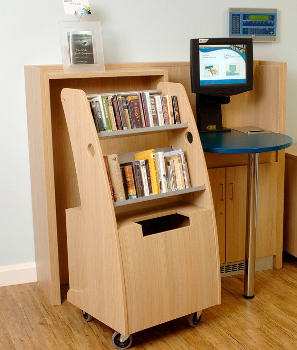 Mobile book return unit with face-out shelving beside a self-service kiosk at Deanshanger Library