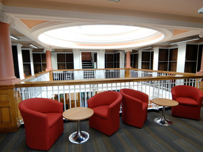 Red tub chairs and side tables overlooking the open-plan library floor at Toxteth Library
