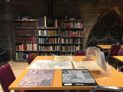 Maps and study tables in a local history area with shelving displaying books at Lichfield Local Studies