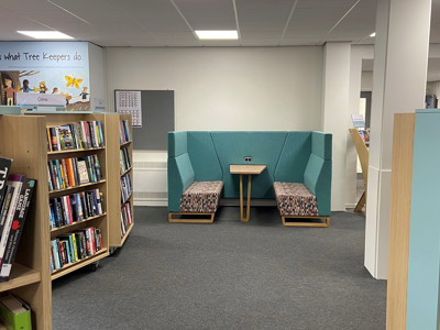 Upholstered seating area with a shared table beside browsing shelves at Blaydon Library