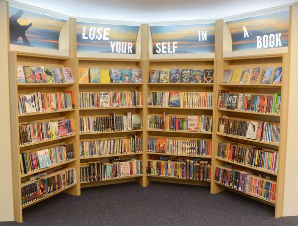 Curved wooden shelving filled with colourful book displays and a backlit sign at Kingham Hill School