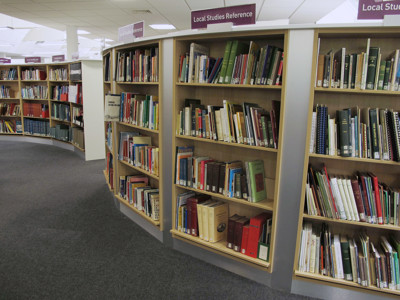 Curved wooden shelving filled with reference books in a local studies area at Newark Local Studies