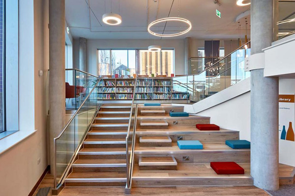 Steps with red and blue upholstered seating create a casual gathering area beside browsing shelves at City Central Library Stoke On Trent