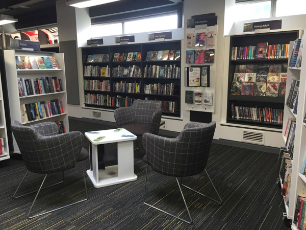 Grey upholstered lounge chairs surrounding a small white table in a young readers' browsing space at Aireborough Library