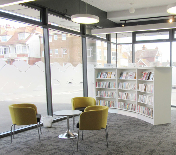 Two yellow lounge chairs and a round table beside a curved book display at Seaford Library