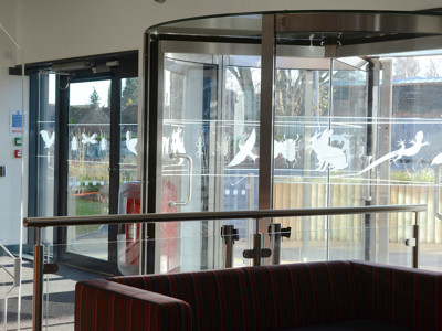 Glass revolving doors with decorative animal silhouettes and a striped sofa in the welcome zone at Brackenhurst Campus Library