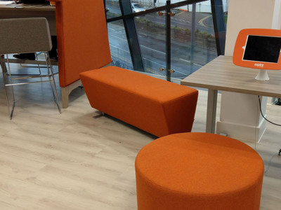 Orange upholstered seating and a round ottoman in a collaborative work area at Newcastle-under-Lyme Library