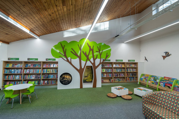 Green tree-shaped wall feature and circular table with green chairs in a children's reading area at Chinnor Library