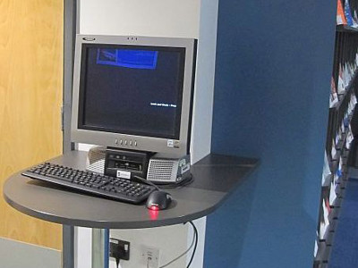 Computer workstation with a curved table beside browsing shelves at Boots Library