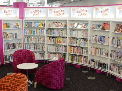 Curved shelving displaying health-themed books and two patterned tub chairs in a wellbeing zone at Southwater Library