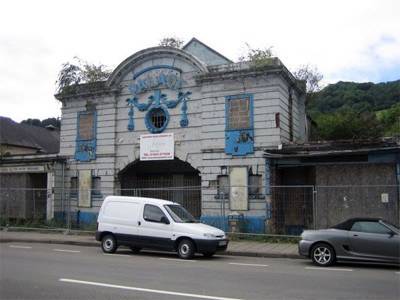 Decaying façade with blue detailing and overgrown vegetation at Risca Palace Library