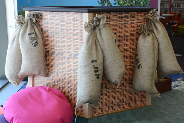 Hessian sacks hanging from a wicker storage unit beside a pink bean bag in a children's play area at Southwater Library