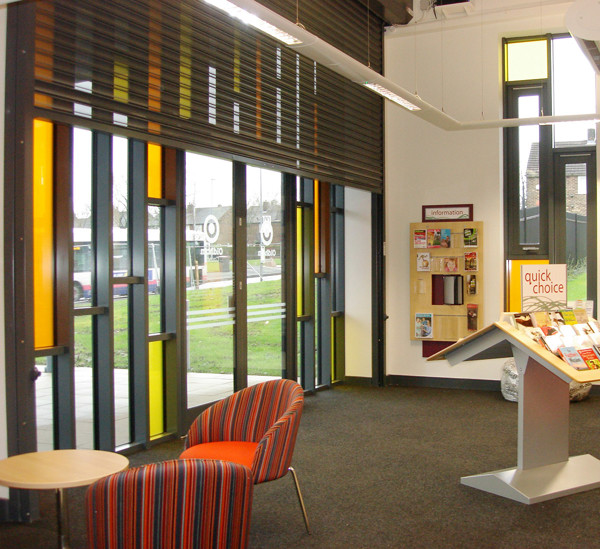 Striped armchair and circular table beside large windows with colourful glass panels at Fitton Hill Library