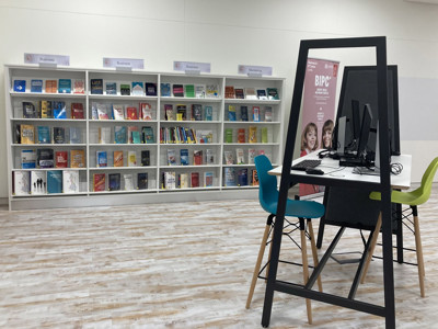 Two study desks with black frames and colourful chairs in a resource area featuring business books at BIPC Leeds
