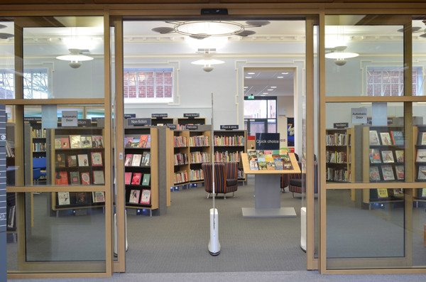 Glass doors leading into a public library browsing area with face-out book displays and striped lounge chairs at Gateshead Central Library