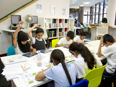 Brightly coloured chairs surround a collaborative work table where children engage in activities using tablets at Redbridge Lab Central