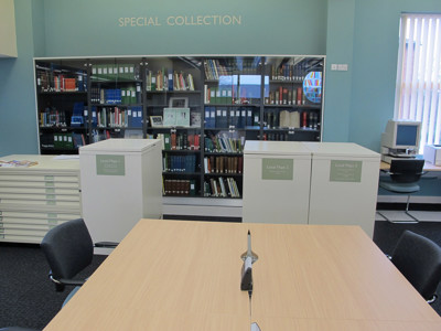 Light wood study tables and grey upholstered chairs in a local studies area featuring a glass-fronted special collection at West Bridgford Local Studies