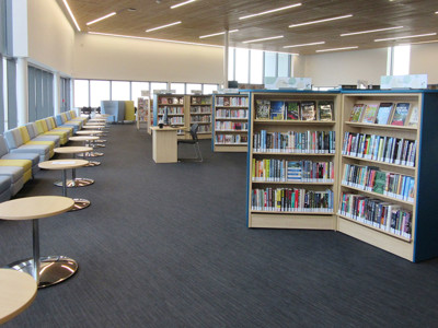Curved shelving units filled with books beside light grey and yellow upholstered seating at Sherwood Library
