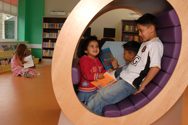 Two children sitting in a circular reading nook, engaged with books, while a third child reads nearby at High Street Library Bolton