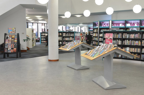 Two angled display stands showcasing face-out book titles in a browsing area with shelving at Redbridge Central Library