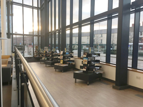 Sunlight streaming through large windows illuminating black shelving units displaying books and products in the retail area at Danum Gallery Library Museum – Shop