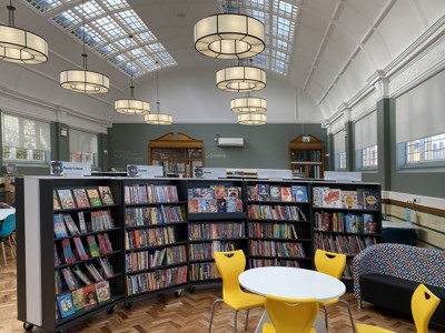 Bright yellow chairs around a circular table beside colourful book displays in a children's reading area at Armley Library