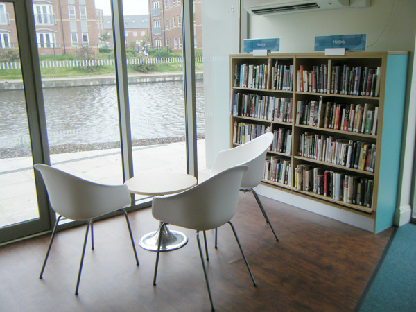 Two white lounge chairs and a small round table beside a history book display at Failsworth Library